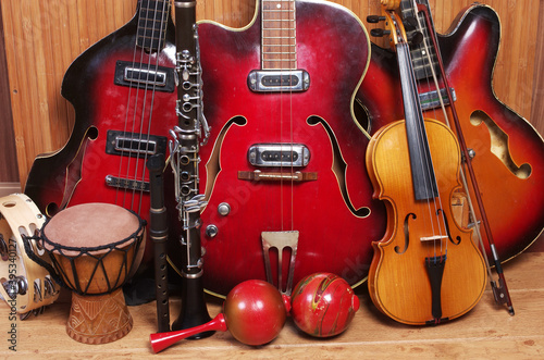 Three vintage electric guitars, violin with bow, clarinet, maracas, djembe on a wooden floor.