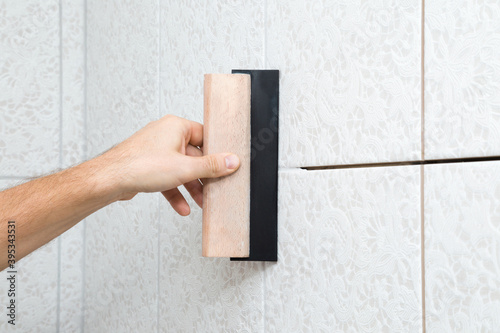 Bild auf Leinwand Worker hand using rubber trowel and grouting seams with paste between ceramic tiles on wall