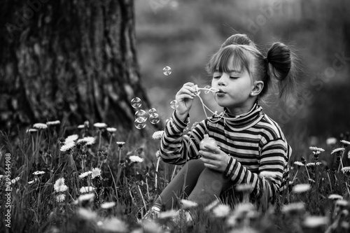 Little cute girl blowing soap bubbles in the park. Black and white photo.