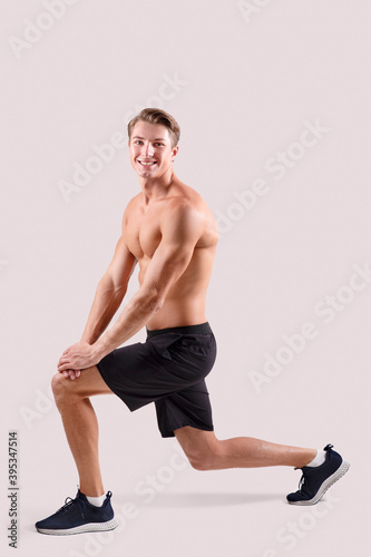 Shirtless millennial guy with bare torso doing lunges on light studio background, full length