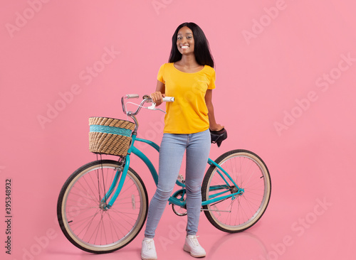 Full length portraif of pretty black lady with vintage bicycle smiling at camera on pink studio background © Prostock-studio