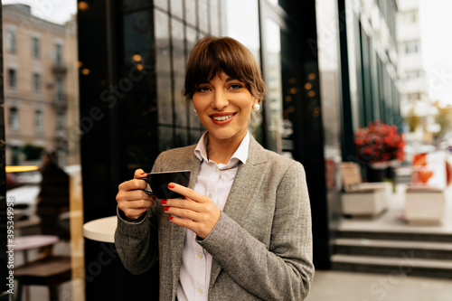 Close up portrait of confident smiling modern business woman with a cup of coffee against the backdrop of a large business building.