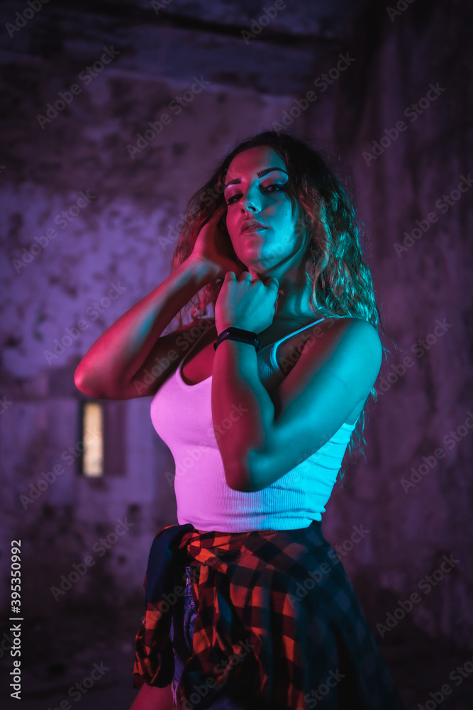 Lifestyle, portrait of a young Caucasian woman in a pose, wearing a tight white shirt and a plaid shirt at the waist. Pink and blue neon lights, urban photography Lifestyle, portrait of a young Caucasian woman in a pose, wearing a tight white shirt and a plaid shirt at the waist. Pink and blue neon lights, urban photography