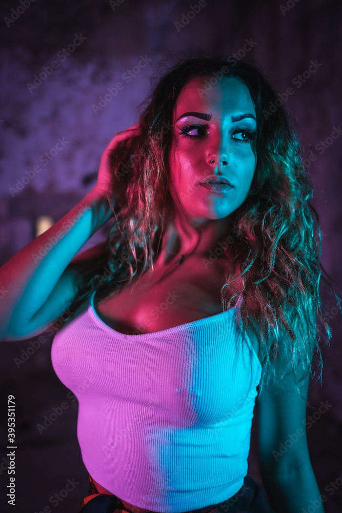 Lifestyle, portrait of a young Caucasian woman in a tight white shirt. Pink and blue neon lights, urban photography of a trap dancer looking sideways Lifestyle, portrait of a young Caucasian woman in a tight white shirt. Pink and blue neon lights, urban photography of a trap dancer looking sideways