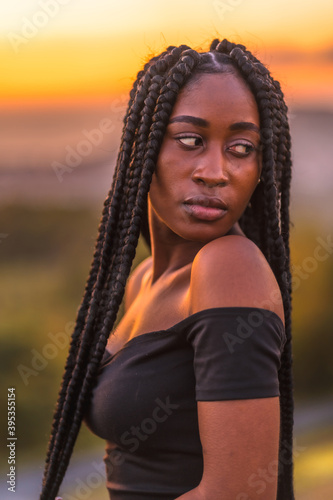 Lifestyle, Latina girl with black skin in a tight black short dress. Portrait of the young man on top of the mountain in a beautiful summer sunset