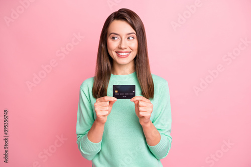Photo of cute funny brunette girl stand show debit card look empty space wear pastel sweater isolated on pink color background