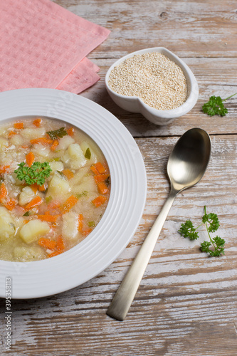 Vegetarian quinoa soup with carrots, potatoes and onions, sprinkled with parsley in a white plate. Vegetable soup with gluten-free quinoa.