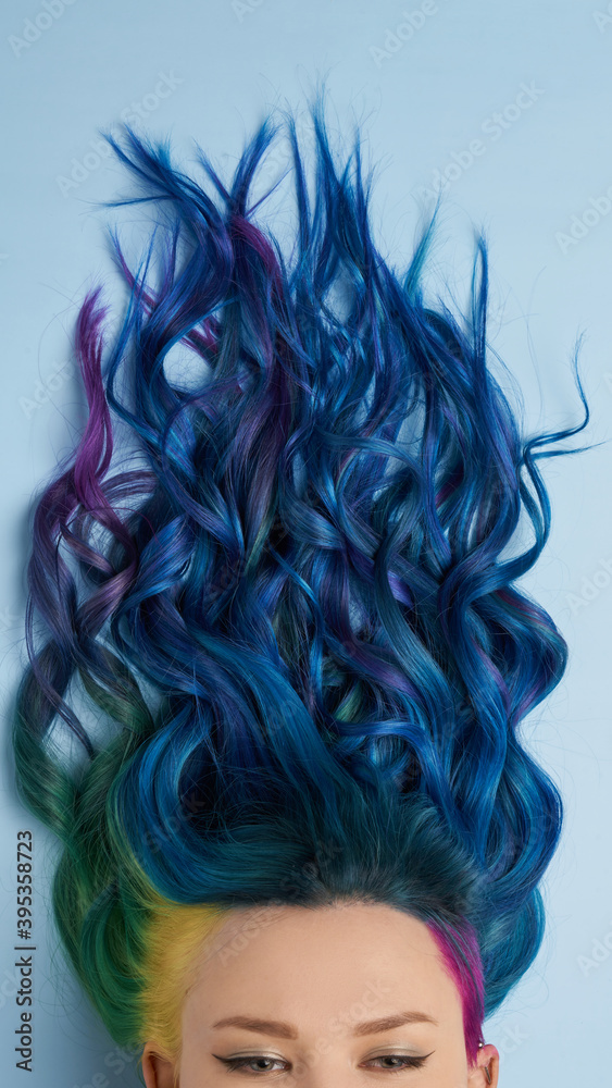 Girl with creative blue coloring and a rainbow in her hair on a blue background. Modern minimalistic bright photography for advertising and social networks Girl with creative blue coloring and a rainbow in her hair on a blue background. Modern minimalistic bright photography for advertising and social networks