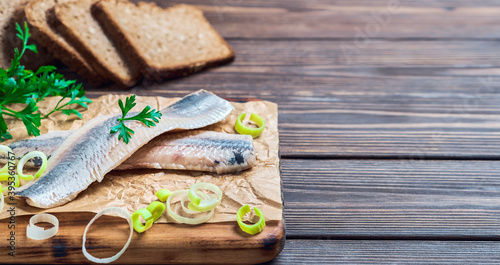 Herring fillet with parsley and onion on a cutting board, close-up, dark wooden background. Traditional Norwegian or Danish smorrebrod ingredients. Herring sandwich, healthy food concept.