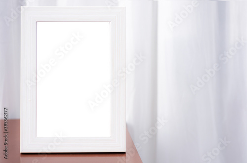 A blank white picture frame perched on the corner of the table. White curtain background in the room