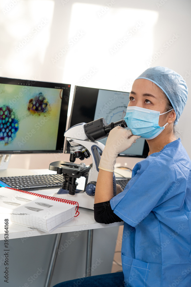 Femme médecin asiatique regarde au microscope des images médicales du covid-19 et de scanner des poumons infectés.