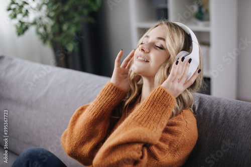 Satisfied pretty lady resting on couch with closed eyes while listening popular music in modern headphones. Concept of relaxation and enjoyment.