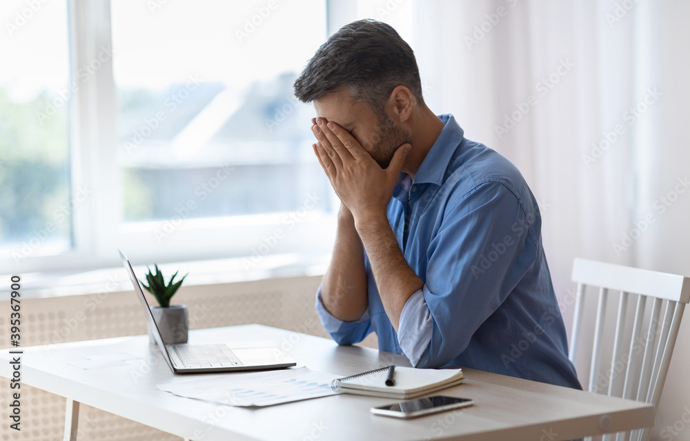Remote Work Stress. Tired freelancer man sitting at desk at home office Remote Work Stress. Tired freelancer man sitting at desk at home office