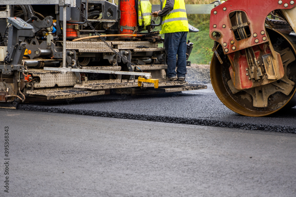 Industrial asphalt paver machine laying fresh asphalt on road construction site. Industrial asphalt paver machine laying fresh asphalt on road construction site.