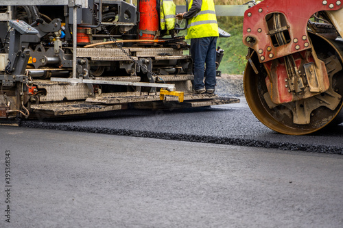 Industrial asphalt paver machine laying fresh asphalt on road construction site.