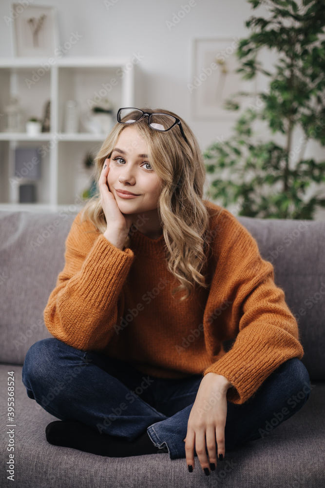 Pretty young lady with wavy blond hair sitting on grey sofa with crossed legs. Time for relaxation at home. Concept of free time. Pretty young lady with wavy blond hair sitting on grey sofa with crossed legs. Time for relaxation at home. Concept of free time.