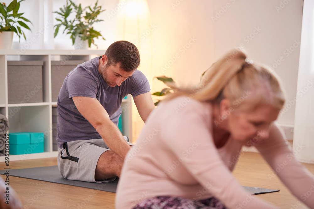 Group Sitting On Exercise Mats Stretching In Yoga Class Inside Community Center Group Sitting On Exercise Mats Stretching In Yoga Class Inside Community Center
