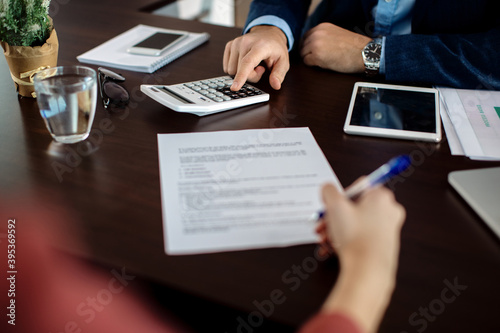 Close-up of insurance agent calculating costs an agreement while having a meeting with a client.
