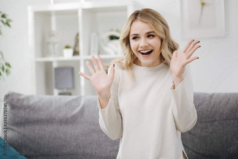 Amazed young blonde in casual clothing sitting on couch with open mouth and gesturing. Charming woman staying at home and feeling shock. Amazed young blonde in casual clothing sitting on couch with open mouth and gesturing. Charming woman staying at home and feeling shock.
