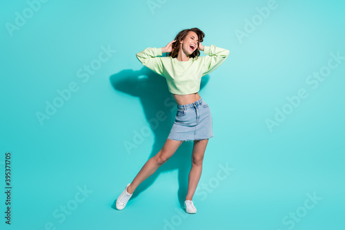 Full length body size photo of cheerful fit girl laughing smiling with closed eyes touching hair isolated on vibrant teal color background