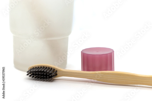 Bamboo wooden eco toothbrushe with charcoal coating, glass cup, toothpaste cap on white background