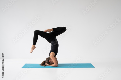Young woman is practicing yoga in a studio. Slim young girl in a black sport wear is doing yoga practice on a blue mat. Concept of healthy life and natural balance between body and mental development.
