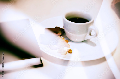 A cup of coffee on a white plate with nuts and chocolate in the glare of light  