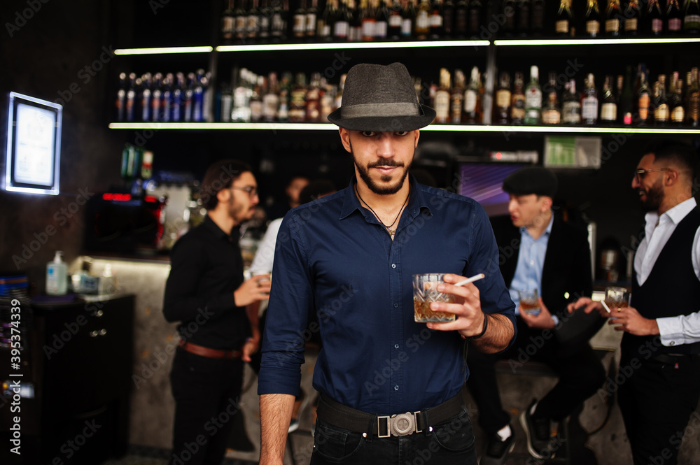 Fototapeta premium Stylish arab man against group of handsome retro well-dressed guys gangsters spend time at club, drinking on bar counter. Multiethnic male bachelor mafia party in restaurant.