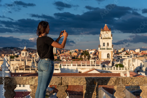 Woman taking pictures of the views over Sucre and its Belltower from a rooftop at Sucre, Bolivia