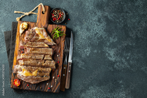 Closeup ready to eat steak ribeye breeds of black Angus with herbs, garlic and butter on a wooden Board. The finished dish for dinner on a dark stone background. Top view with copy space