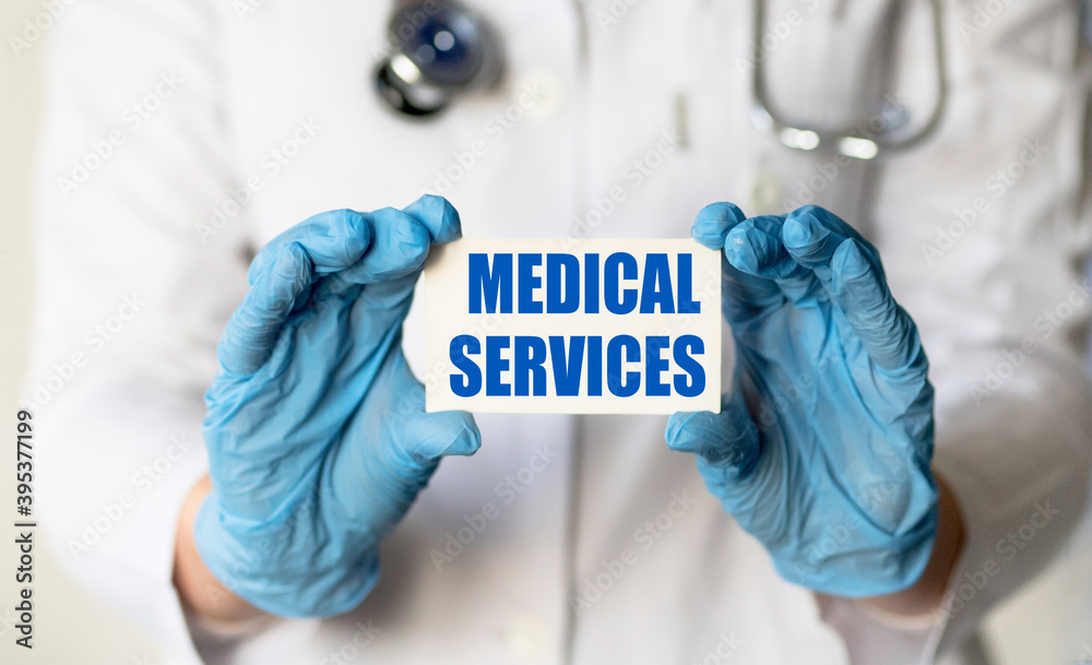 A medical worker in gloves holds a card with the words MEDICAL SERVICES. Medical concept. A medical worker in gloves holds a card with the words MEDICAL SERVICES. Medical concept.