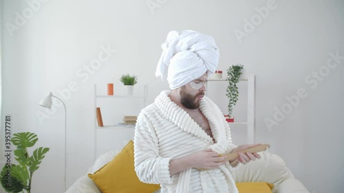 Carefree funny young man having fun dancing alone at home in a bathrobe and a towel on his head