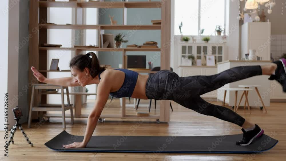 A young fit athletic girl works out her abdominal muscles using a workout on the phone. Woman doing sports and fitness at home during covid quarantine. Healthy lifestyle during a pandemic A young fit athletic girl works out her abdominal muscles using a workout on the phone. Woman doing sports and fitness at home during covid quarantine. Healthy lifestyle during a pandemic