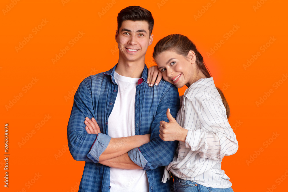 Smiling man and lady in casual clothes, look at camera, female presses to guy shoulder and shows thumb up Smiling man and lady in casual clothes, look at camera, female presses to guy shoulder and shows thumb up