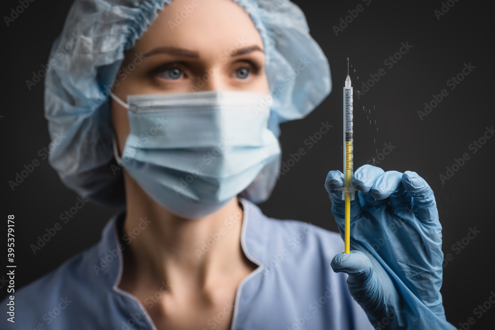 syringe with vaccine splash in hand of nurse in medical mask on blurred background isolated on dark syringe with vaccine splash in hand of nurse in medical mask on blurred background isolated on dark