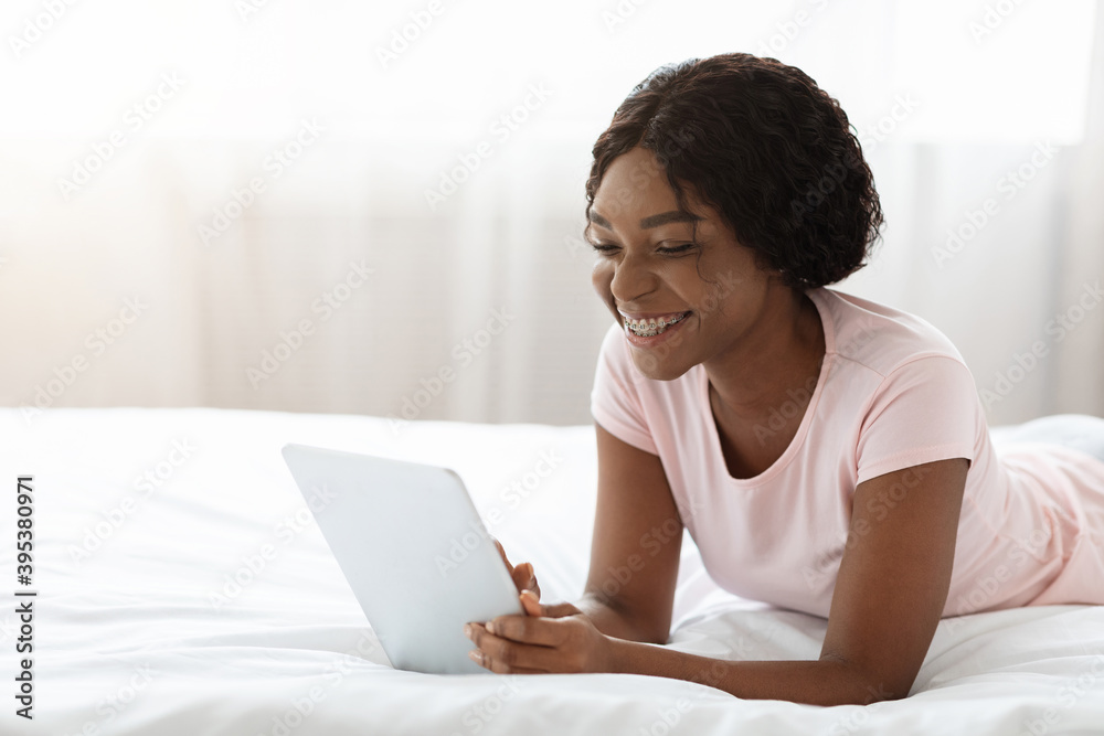 Happy african lady enjoying weekend, laying with pad on bed Happy african lady enjoying weekend, laying with pad on bed