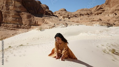 Pretty woman grabs a handful of dry sand and lets it fall between her fingers. Young traveler sitting in sunny desert dune and sifting particles fronm her hands. photo