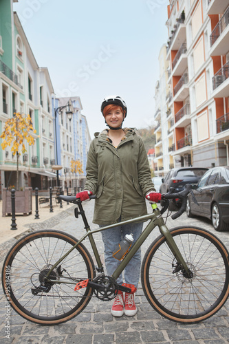Fototapeta Naklejka Na Ścianę i Meble -  Vertical full length shot of a lovely young stylish woman posing with her bicycle, wearing protective helmet