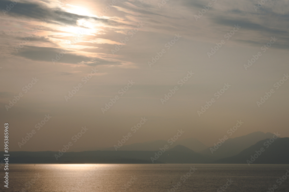 Sunset at Garda lake, Italy. Sun behind clouds with reflections. 