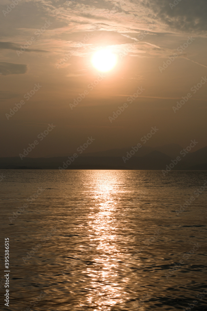 Sunset at Garda lake, Italy. Sun behind clouds with reflections. 