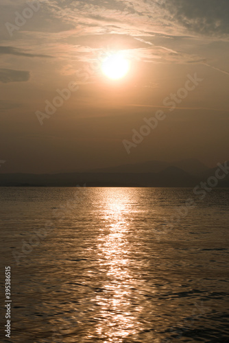Sunset at Garda lake  Italy. Sun behind clouds with reflections. 