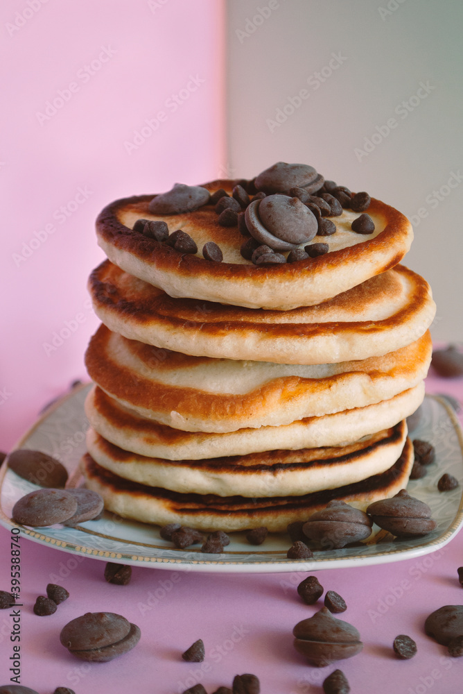 Pancakes close up with round chocolate pieces on top and around on a pink surface.