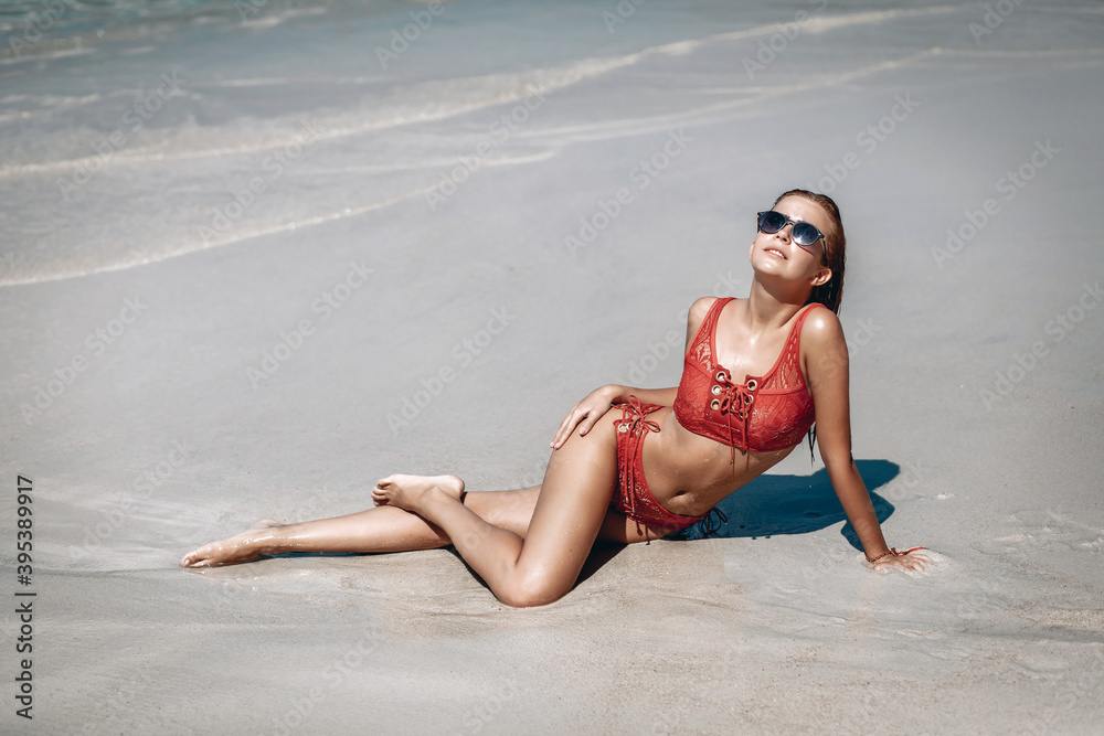 Gorgeous red-haired woman with sexy body dressed in red bikini  and sunglass lying on the beach, seductive female in swimsuit rest after swimming. Phuket. Thailand
