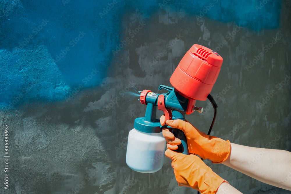 Painting a roughly plastered wall with a hand-held spray gun. Spray gun  without hose with overhead compressor. Stock Photo | Adobe Stock