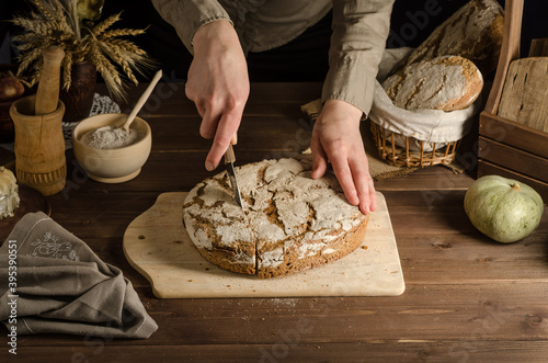 A woman is slicing freshly baked whole grain homemade rye bread.