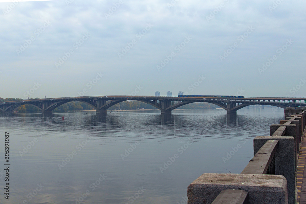 Fototapeta premium Scenic morning landscape view Dnieper River. Metro (Subway) Bridge over Dnipro River. The metro train moves on the bridge. Nature landscape with autumn colors. Kyiv, Ukraine