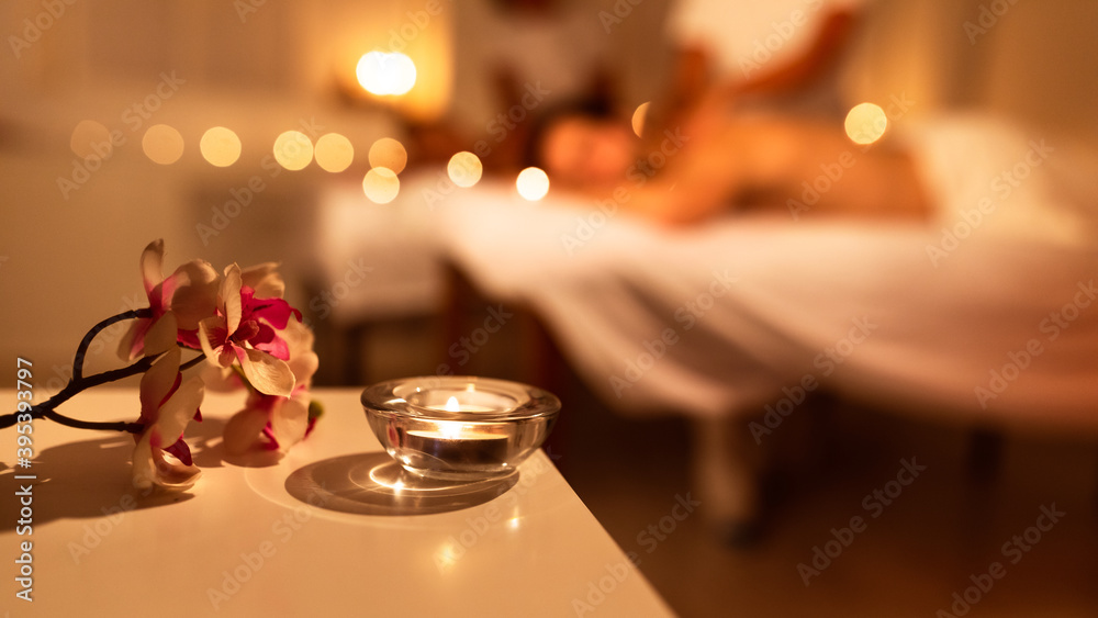 Couple Receiving Massage Indoor, Spa Composition With Candle And Flowers Couple Receiving Massage Indoor, Spa Composition With Candle And Flowers