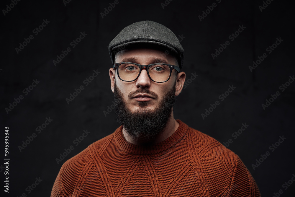 Headshot of bearded hipster posing in dark background weared with glasses and cap. Headshot of bearded hipster posing in dark background weared with glasses and cap.