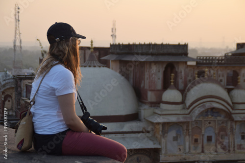 Photography Young woman and solo traveler, sitting on the rooftop watching the sunset over the city skyline with a camera around her neck