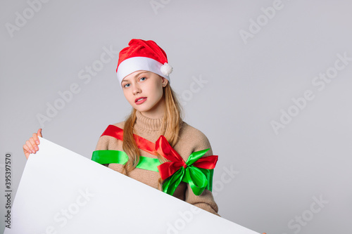 Slika na platnu A cute girl in a santa hat holds a white banner where your advertisement can be